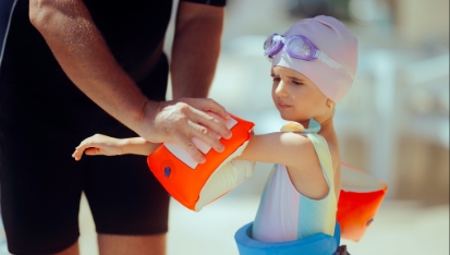  Swimming Instructor Helps Student Put on Inflatable Arm Floaties Little child wearing protective gear for her swimming lesson in the pool