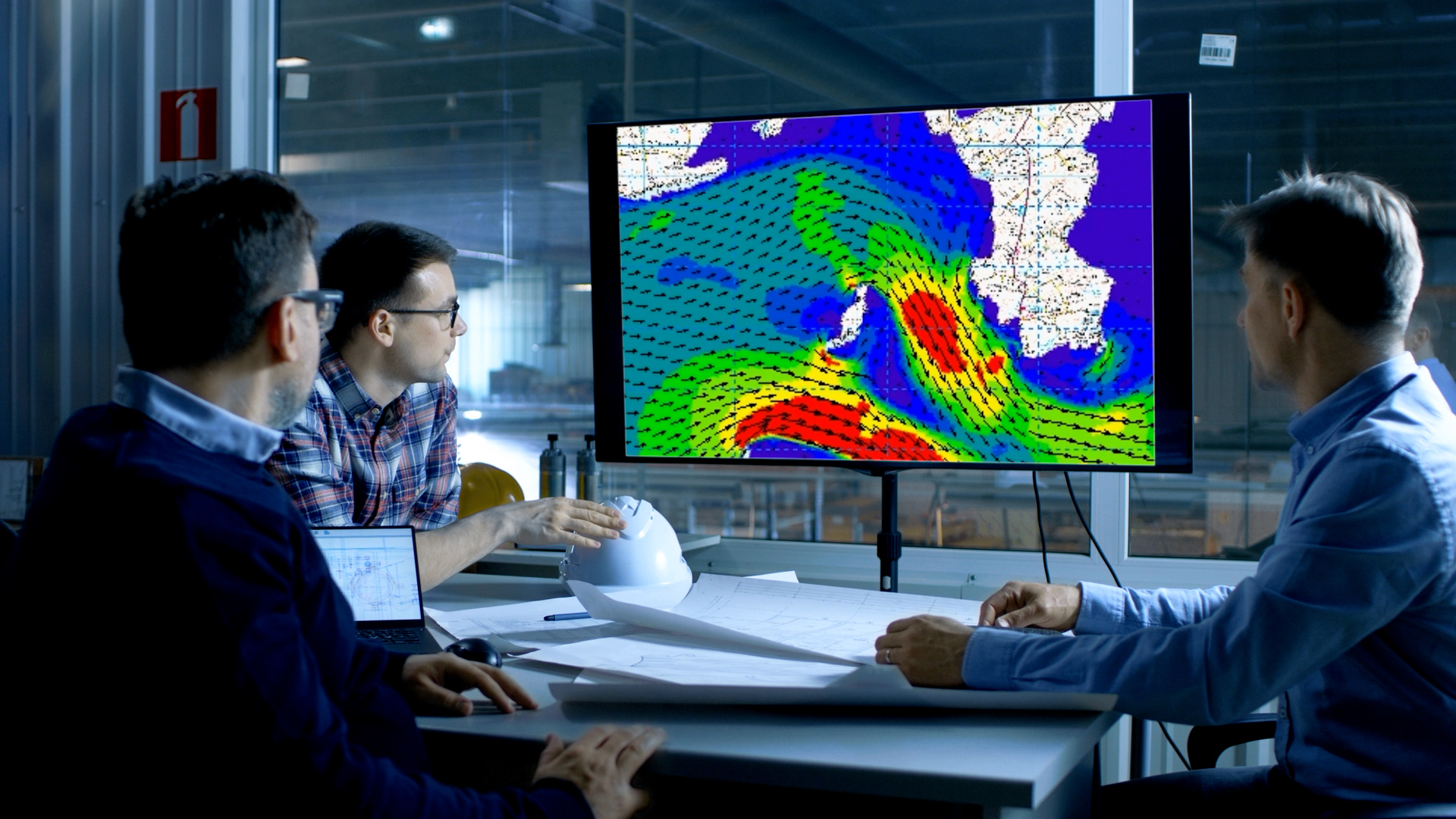 3 people sitting at an office table looking at a large computer monitor that shows a computer-generated body of water