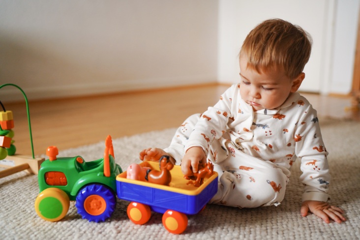 Young boy playing with toy cars indoors, sitting on the floor on a carpet.