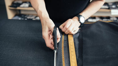 Osoba cięcie tkaniny nożyczkami, mierzenie za pomocą linijki podczas produkcji odzieży.