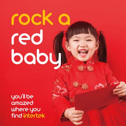 A broadly smiling young Asian girl dressed in red and holding a red envelope